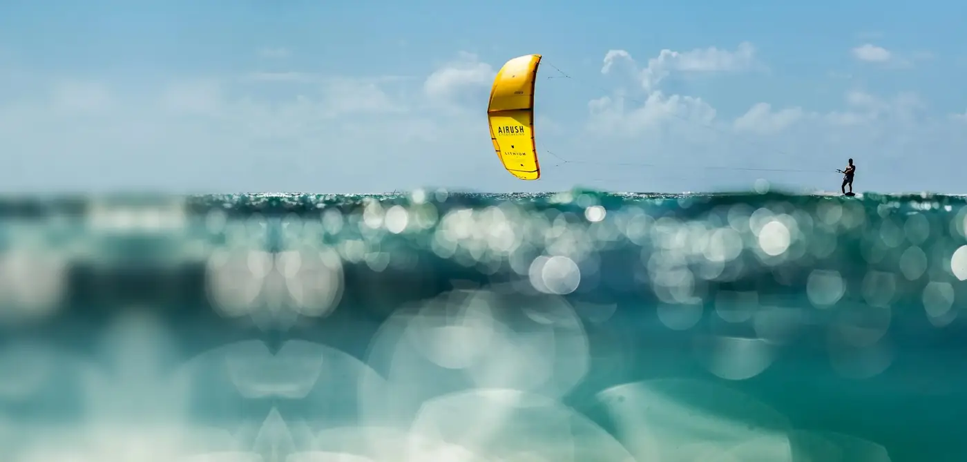 Kitesurfista con una cometa amarilla Airush Lithium deslizándose sobre agua turquesa