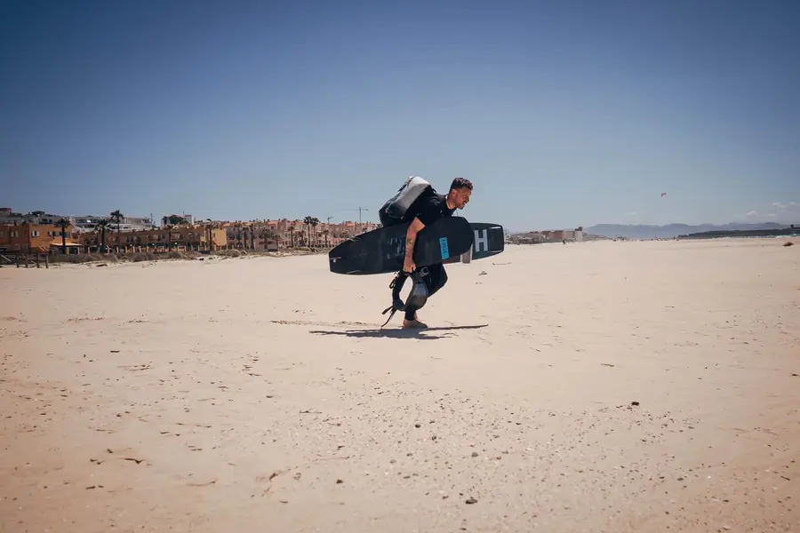 Kitesurfista con tabla y mochila de cometa caminando por la playa de Tarifa