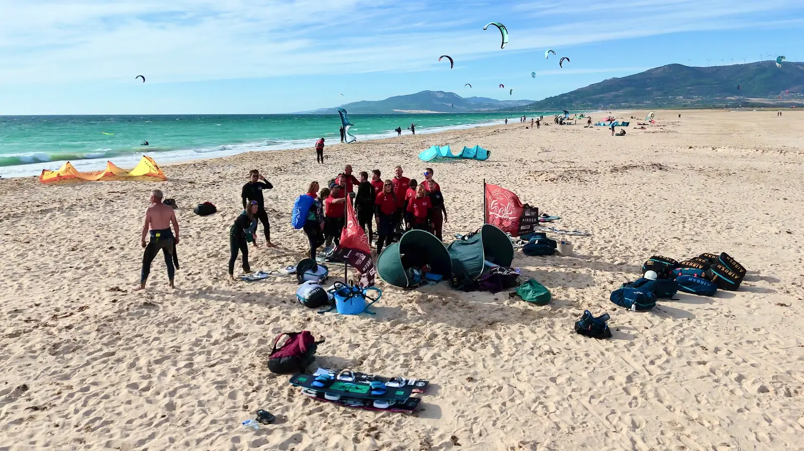 Grupo del kite camp con licras rojas celebrando en la playa de Los Lances, con muchas cometas